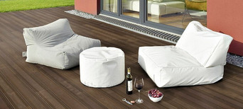 Terrasse mit dunklen Thermo-Esche-Dielen, bequemen Sitzsäcken, weißem Pouf und stilvoll arrangiertem Wein und Snacks.